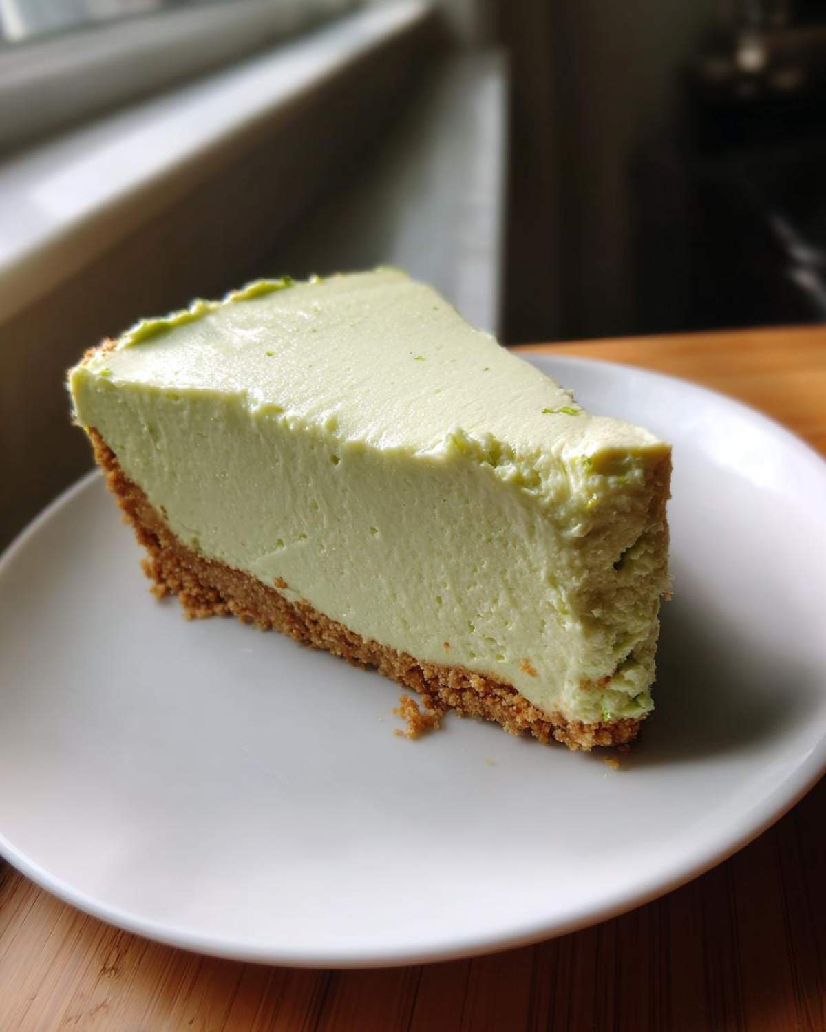 A thick slice of creamy, pale green no-bake key lime cheesecake with a graham cracker crust on a white plate.