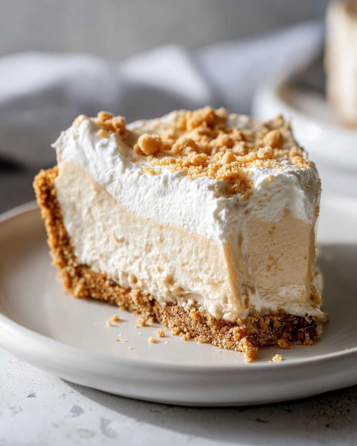 Close-up of a creamy slice of peanut butter pie with a thick graham cracker crust and whipped topping sprinkled with crumbs.