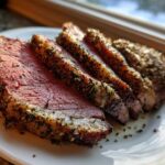 Four thick slices of perfectly cooked rib roast showing a medium-rare center and a heavily seasoned herb crust, resting on a white plate.