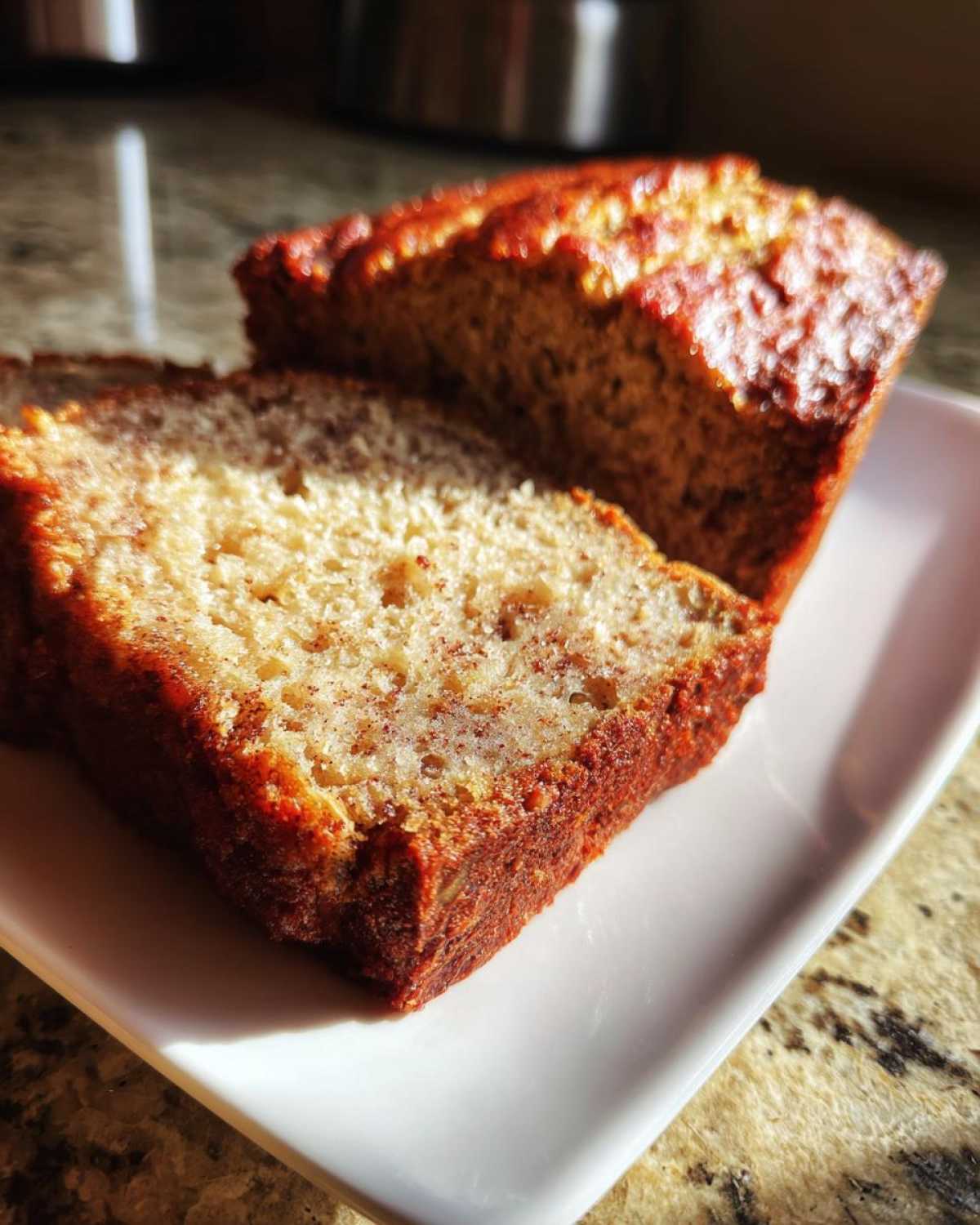 Close-up of two slices of moist sugar free banana bread with a golden-brown crust on a white plate.