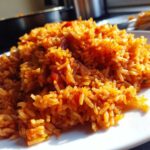 A close-up, appetizing shot of perfectly cooked, vibrant orange smoky jollof rice served on a white plate.