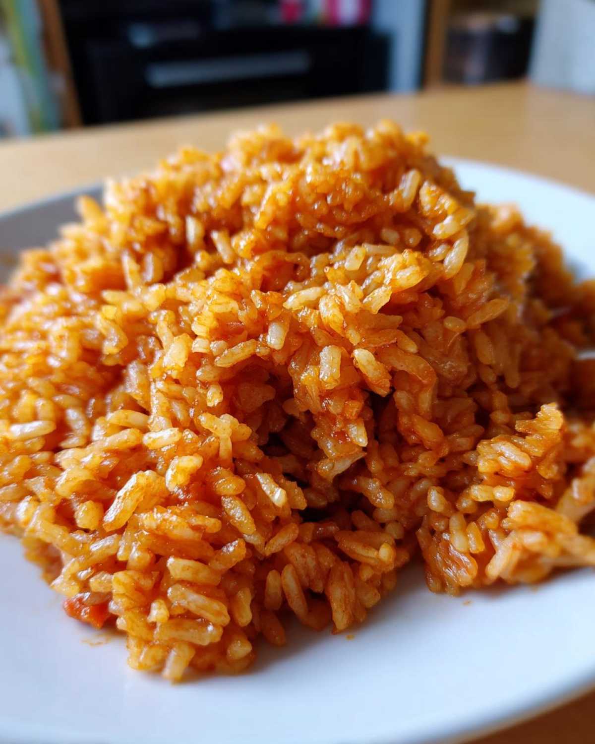 A close-up, appetizing shot of perfectly cooked, smoky jollof rice piled high on a white plate.