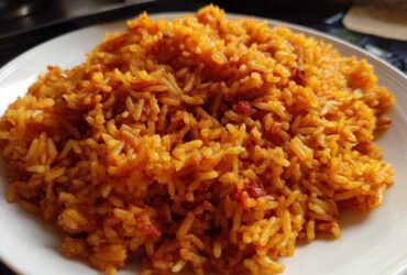 A close-up image showing a generous serving of vibrant, orange-red smoky jollof rice piled on a white plate.