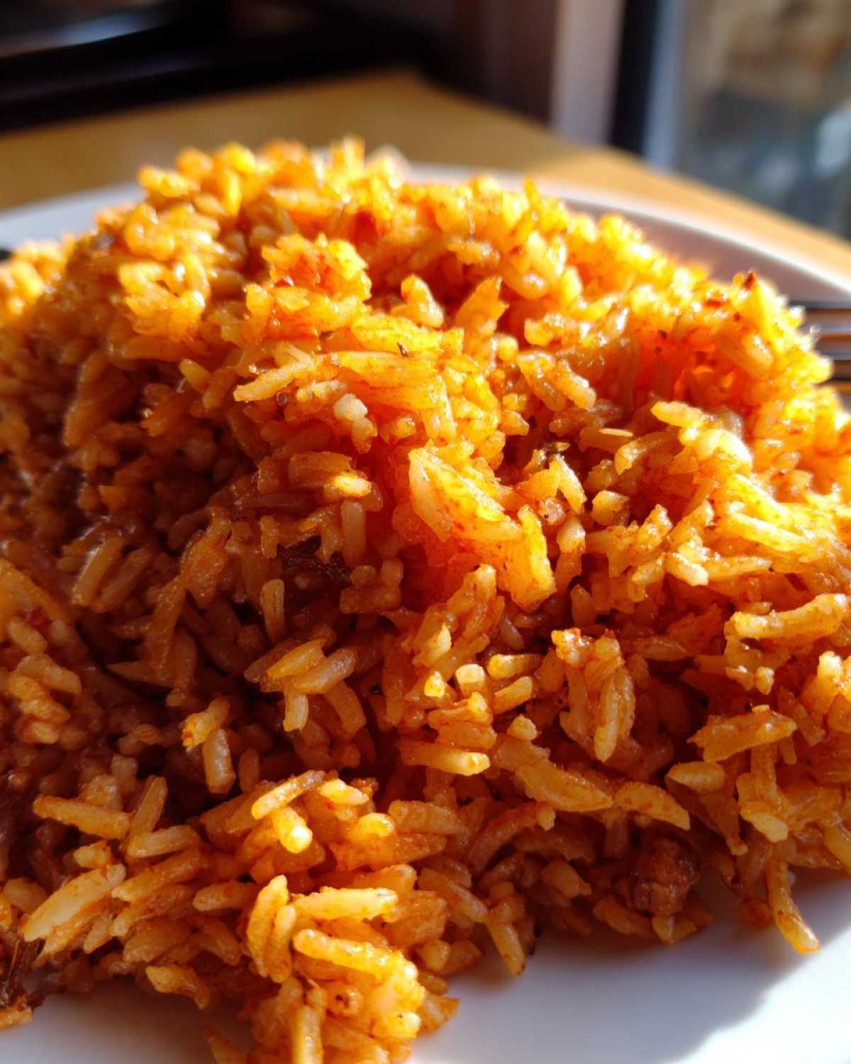 Close-up, vibrant image of perfectly cooked, smoky jollof rice piled high on a white plate.