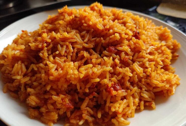 A close-up image showing a generous serving of vibrant, orange-red smoky jollof rice piled on a white plate.