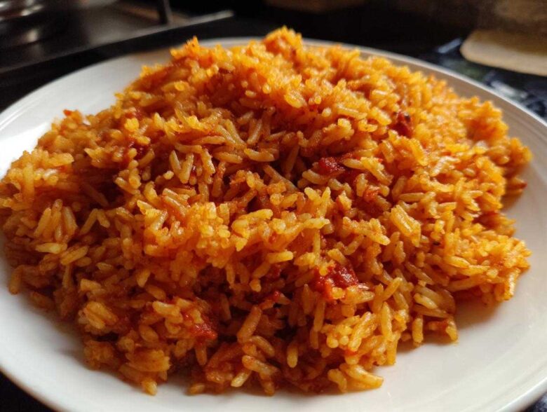 A close-up image showing a generous serving of vibrant, orange-red smoky jollof rice piled on a white plate.