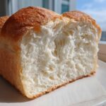 Close-up of a freshly baked loaf of condensed milk bread, showing its incredibly soft, white, fluffy interior crumb.