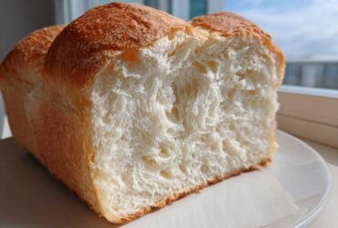 Close-up of a freshly baked loaf of condensed milk bread, showing its incredibly soft, white, fluffy interior crumb.