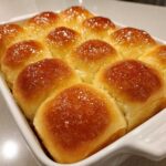 A close-up of twelve golden brown, soft dinner rolls baked together and brushed with a shiny glaze.