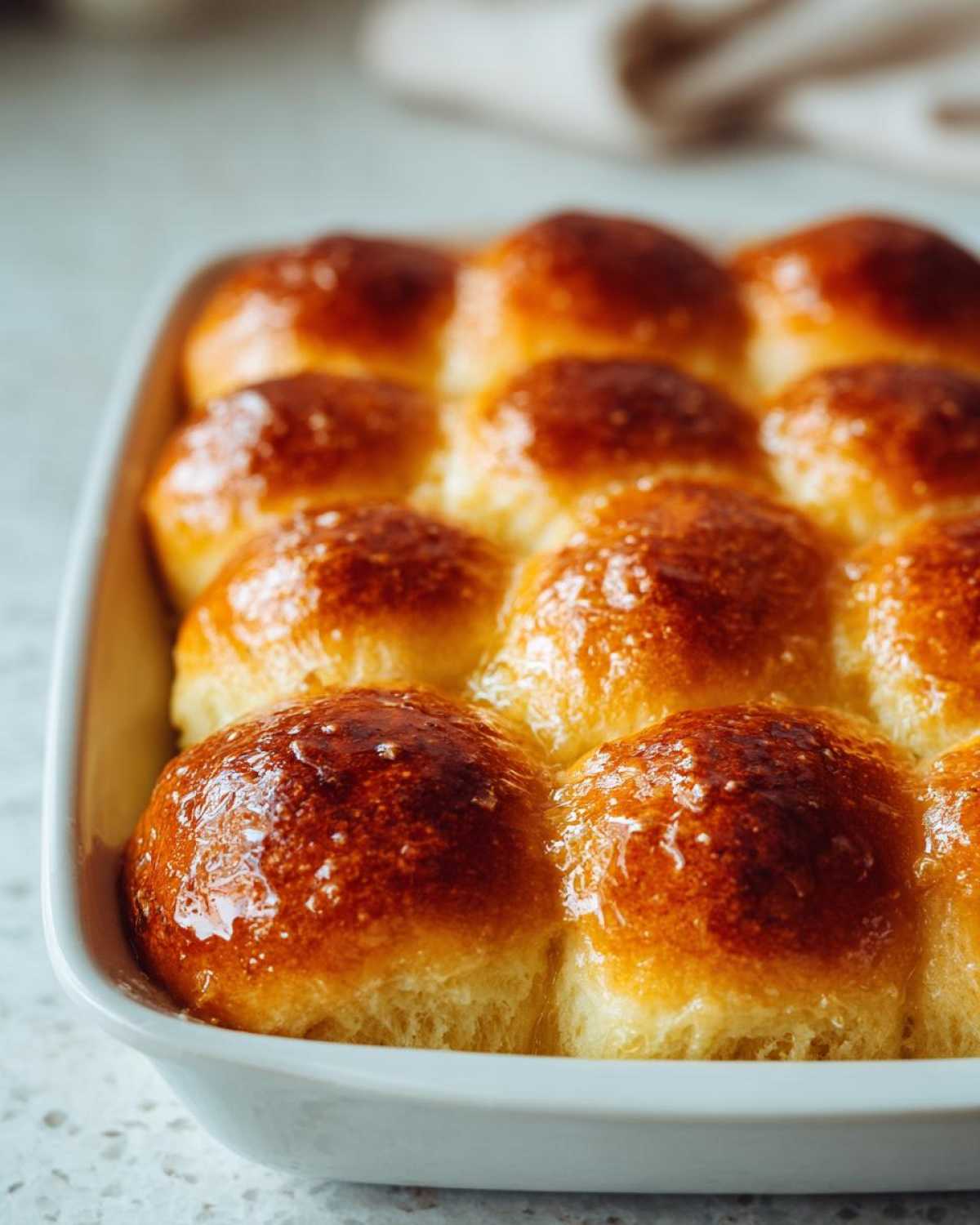 Close-up of twelve golden brown, shiny dinner rolls baked together in a white dish.