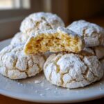 Close-up of soft lemon crinkle cookies, one broken in half to show the bright yellow, chewy interior.
