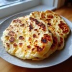 Two pieces of freshly cooked, soft naan bread with golden brown and charred spots served on a light gray plate.