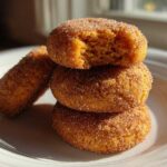A stack of three soft pumpkin snickerdoodle cookies coated in cinnamon sugar, with the top one having a bite taken out.