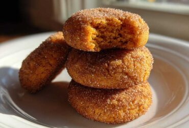 A stack of three soft pumpkin snickerdoodle cookies coated in cinnamon sugar, with the top one having a bite taken out.