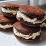 Close-up of stacked, soft tiramisu cookies featuring dark cocoa shells and thick, creamy white filling dusted with cocoa powder.