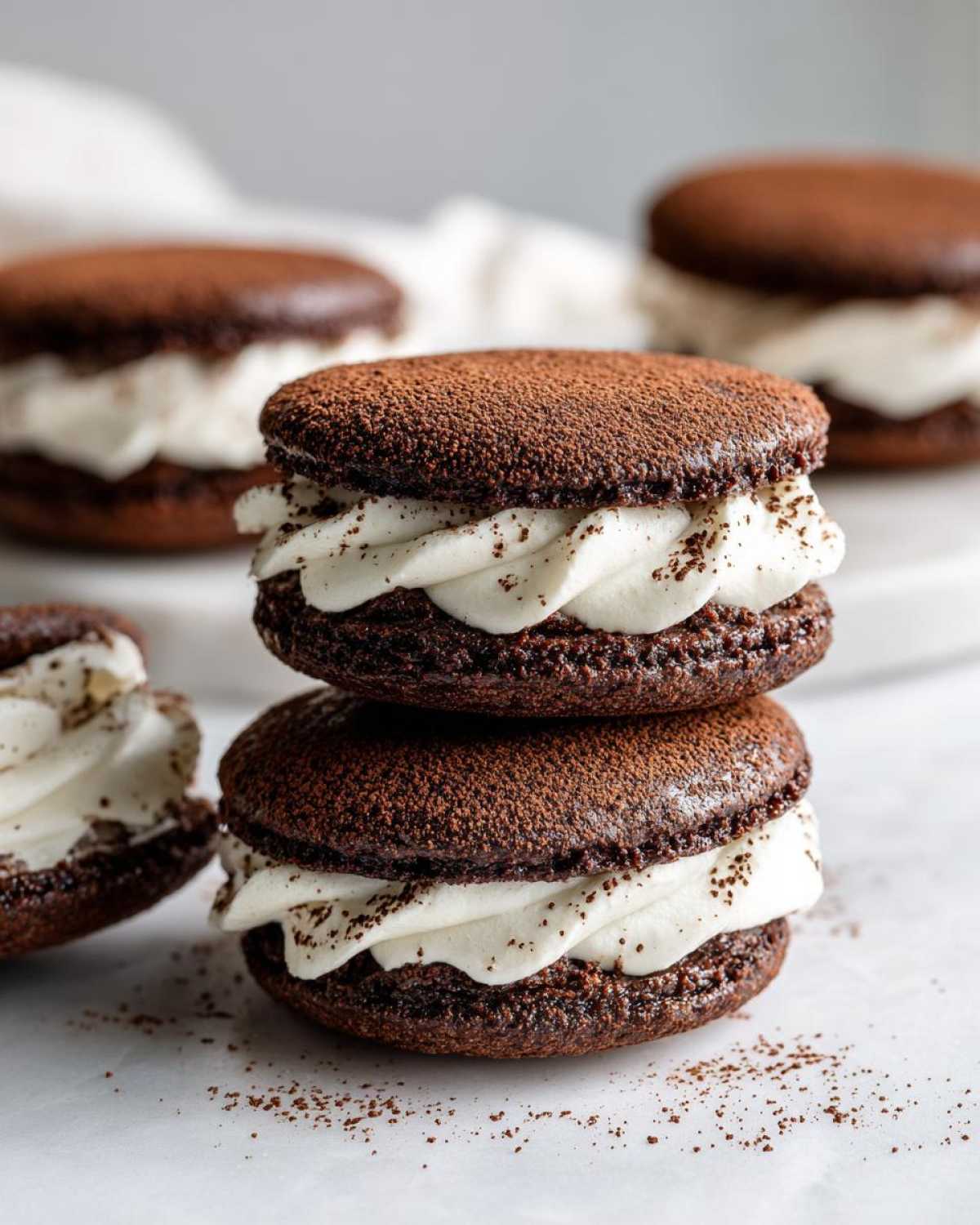 Two soft tiramisu cookies stacked, featuring dark chocolate shells and thick white cream filling, dusted with cocoa powder.