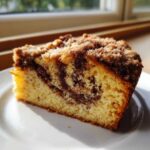 A close-up slice of moist sour cream coffee cake featuring a rich cinnamon swirl and crumb topping.