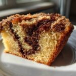 Close-up of a moist slice of sour cream coffee cake showing the yellow cake base, dark cinnamon swirl, and crumbly streusel topping.
