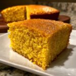 A close-up view of a moist, golden slice of sourdough cornbread on a white plate.