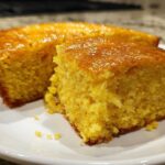 Close-up of a moist, golden slice of sourdough cornbread with a shiny, glazed top.