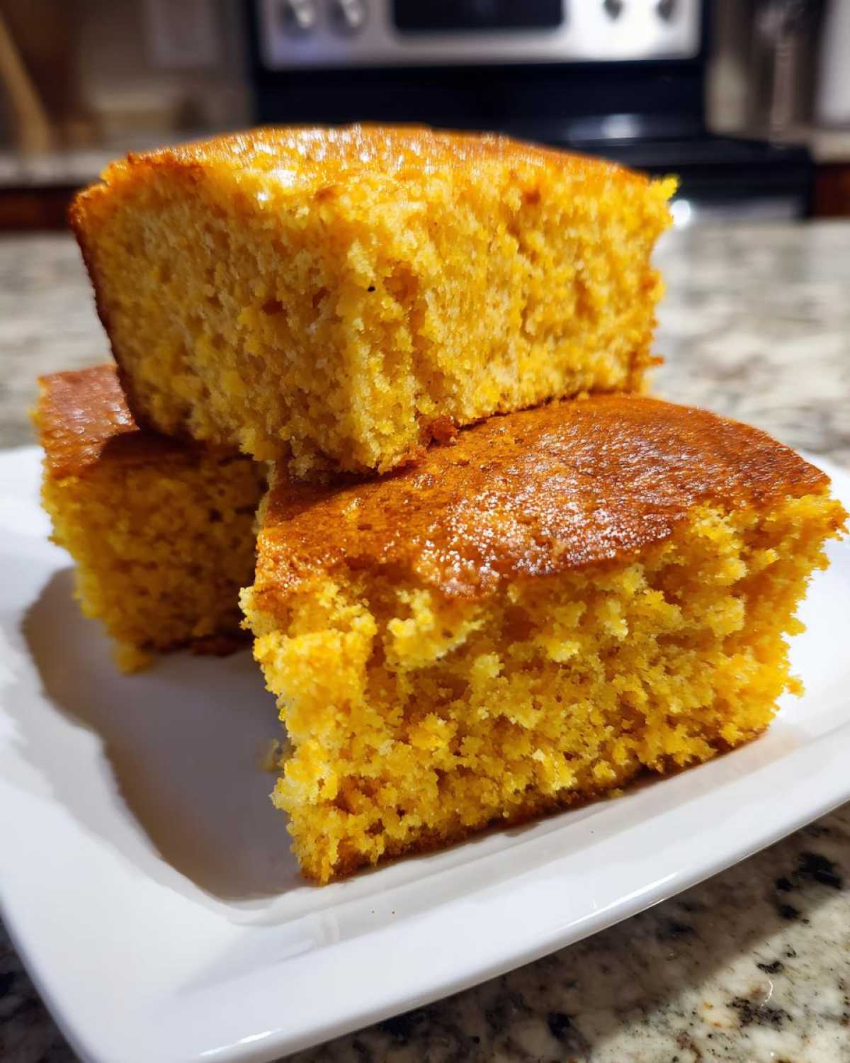 Three golden-brown squares of moist sourdough cornbread stacked on a white plate.
