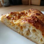 Close-up cross-section showing the airy crumb structure of sourdough discard pizza dough topped with melted, browned cheese.