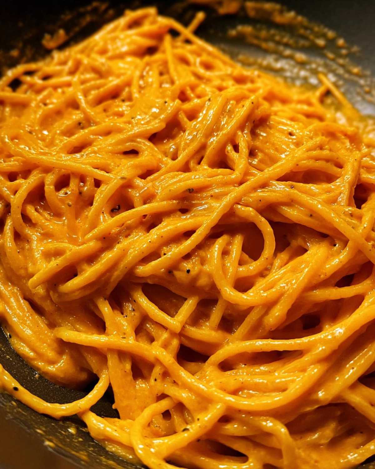 Close-up of spaghetti noodles thoroughly coated in a creamy, vibrant orange butternut squash pasta sauce.