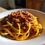 A close-up of spaghetti generously topped with rich, meaty bolognese sauce served in a white bowl.