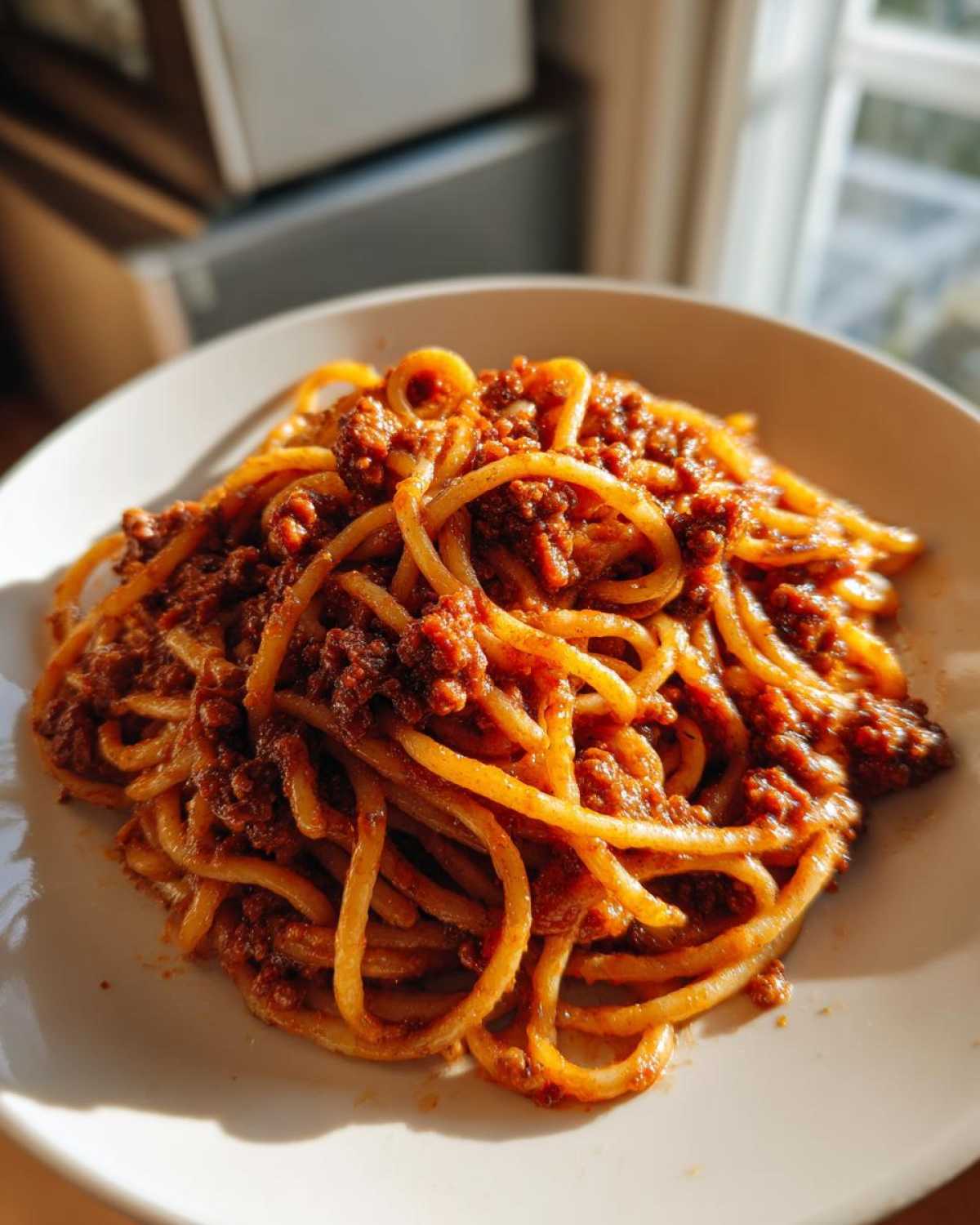 A close-up of spaghetti heavily coated in a rich, meaty bolognese sauce served on a white plate.