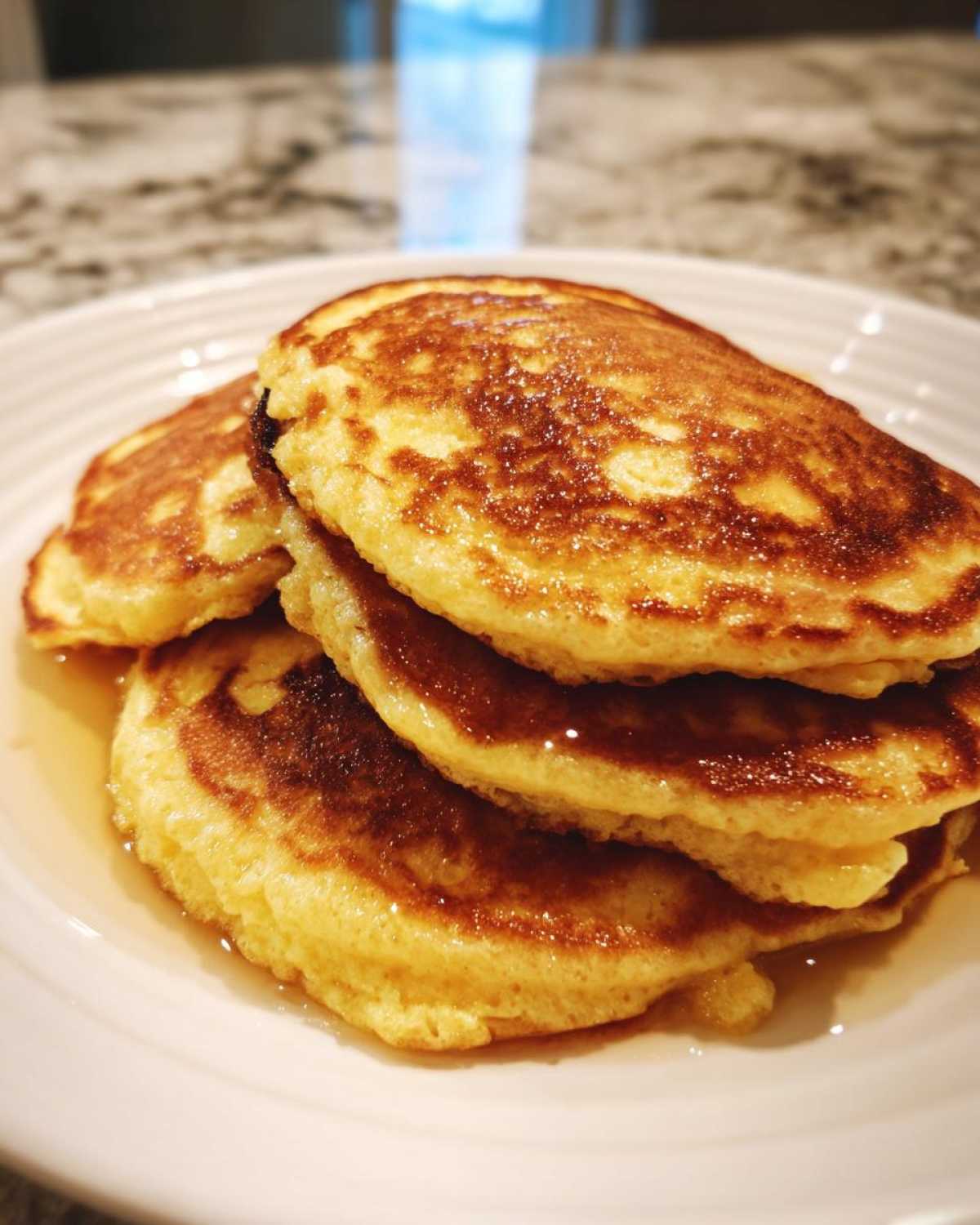 A close-up stack of three golden brown almond flour pancakes drizzled with syrup on a white plate.