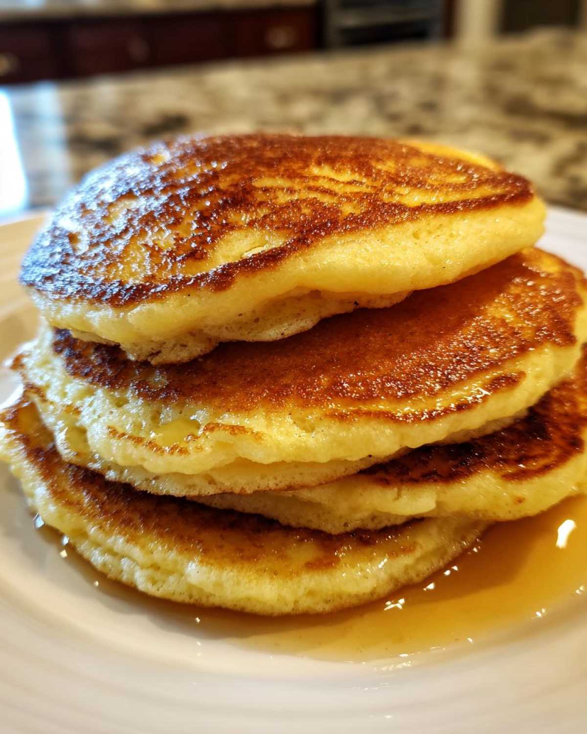 A stack of three golden brown almond flour pancakes drizzled with syrup on a white plate.