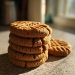 A stack of four perfectly textured Easy Peanut Butter Cookies with fork marks, sitting on a counter in warm sunlight.