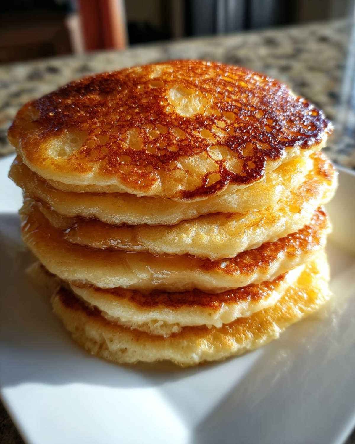 A tall stack of five fluffy sourdough pancakes glistening with syrup on a white plate.