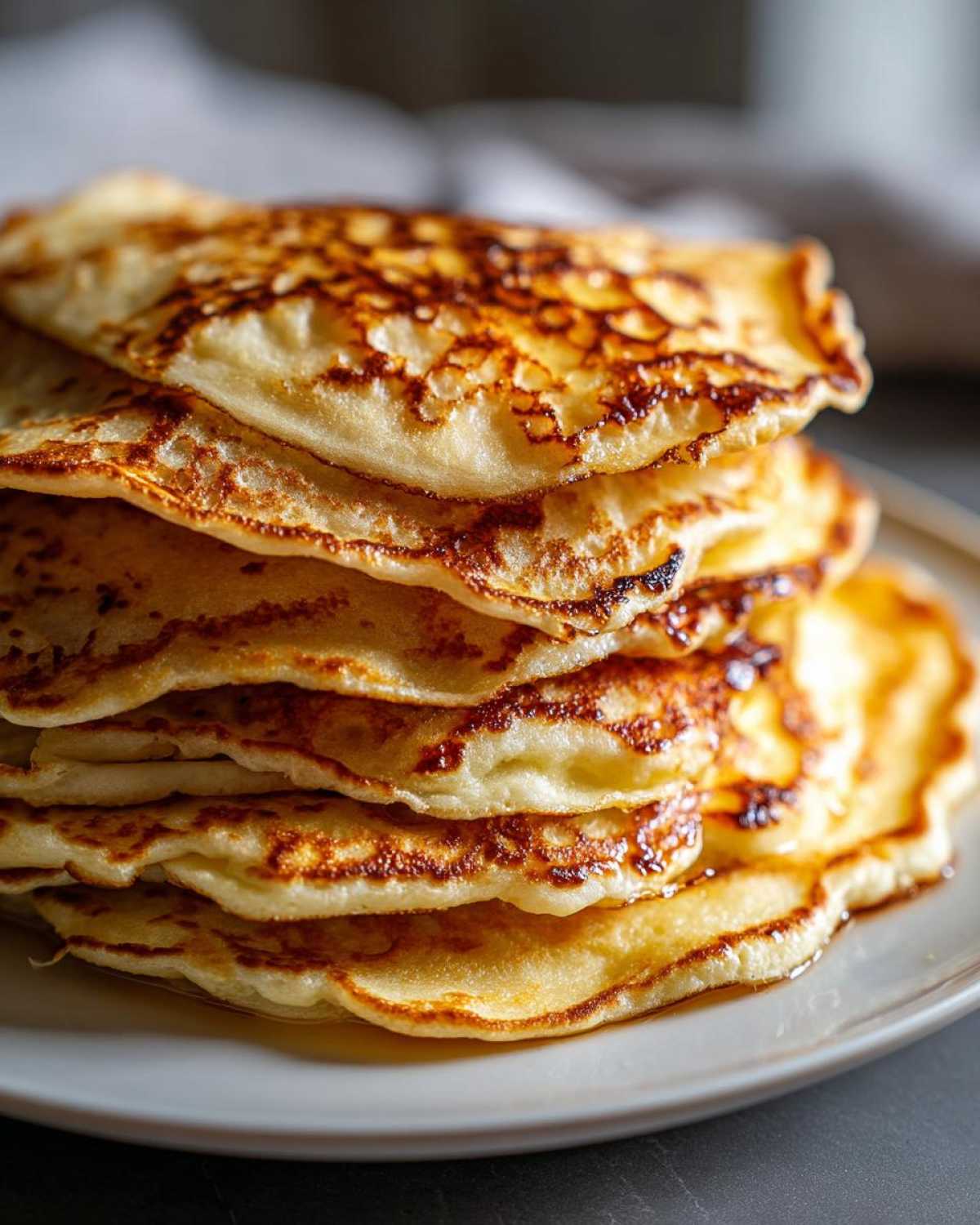 A tall stack of fluffy, golden-brown sourdough pancakes drizzled with syrup on a light plate.