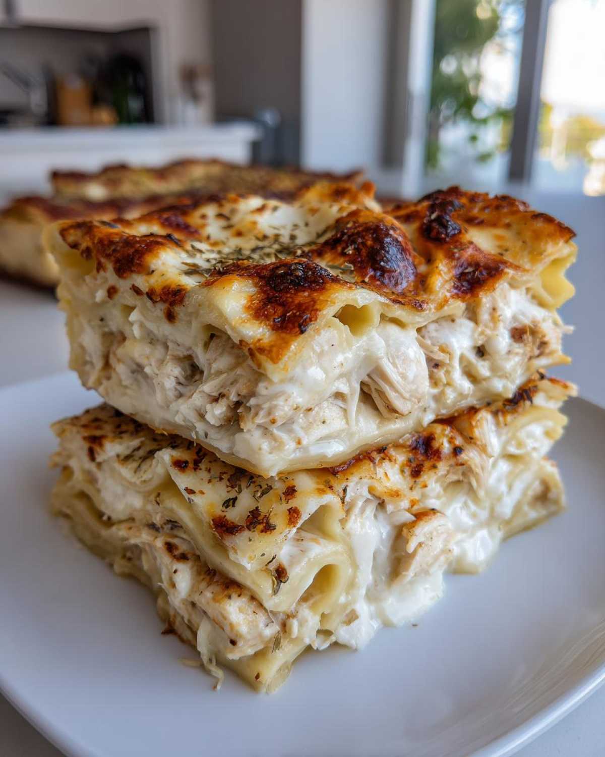 Two stacked, thick slices of creamy chicken alfredo lasagna showing layers of pasta, shredded chicken, and a browned, cheesy top.