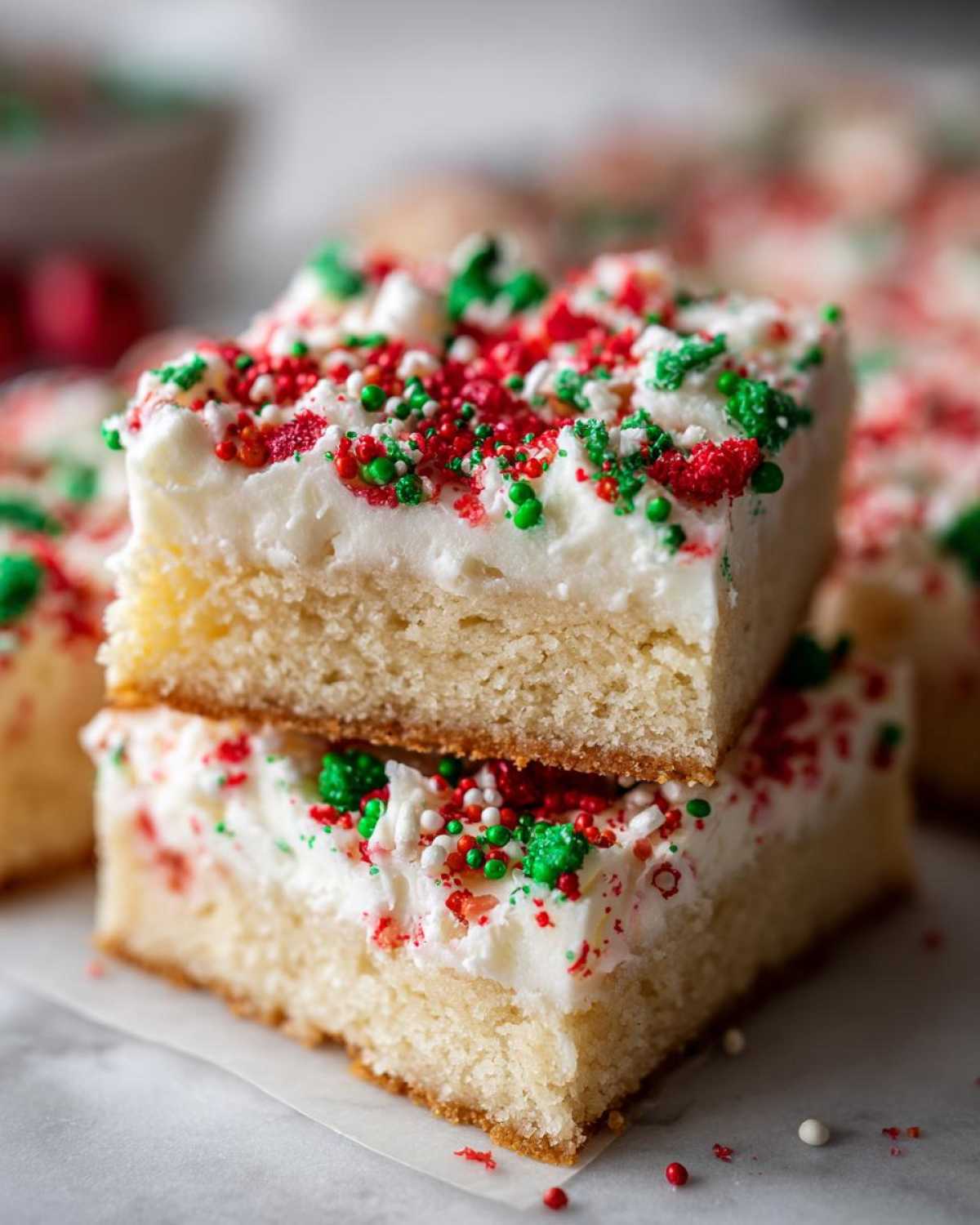 Two stacked squares of thick christmas sugar cookie bars topped with white frosting and red and green sprinkles.