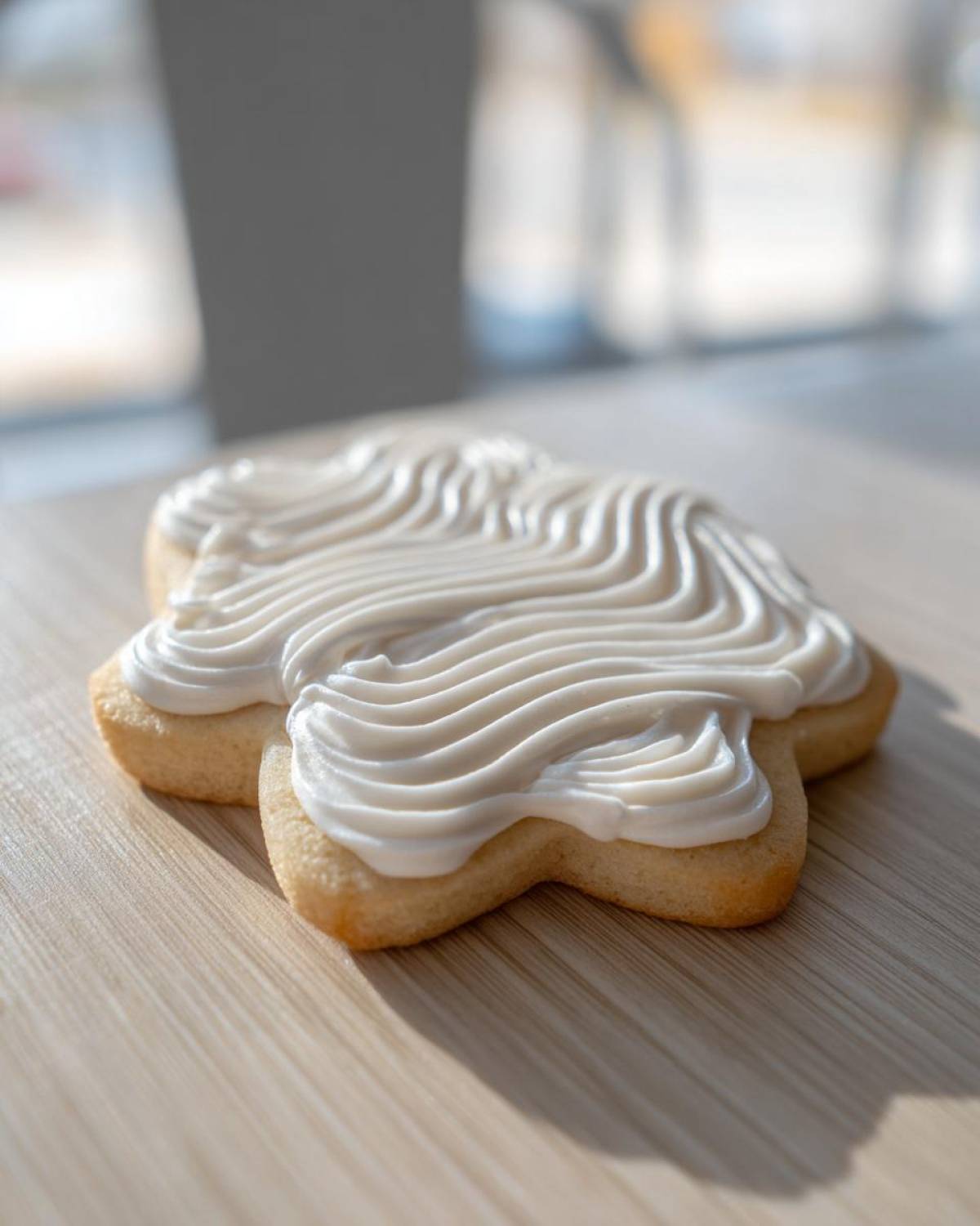 A star-shaped sugar cookie topped with thick, white, piped sugar cookie icing recipe frosting, sitting on a wooden surface.
