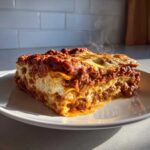 A thick, steaming slice of homemade lasagna with rich meat sauce and melted cheese on a white plate.