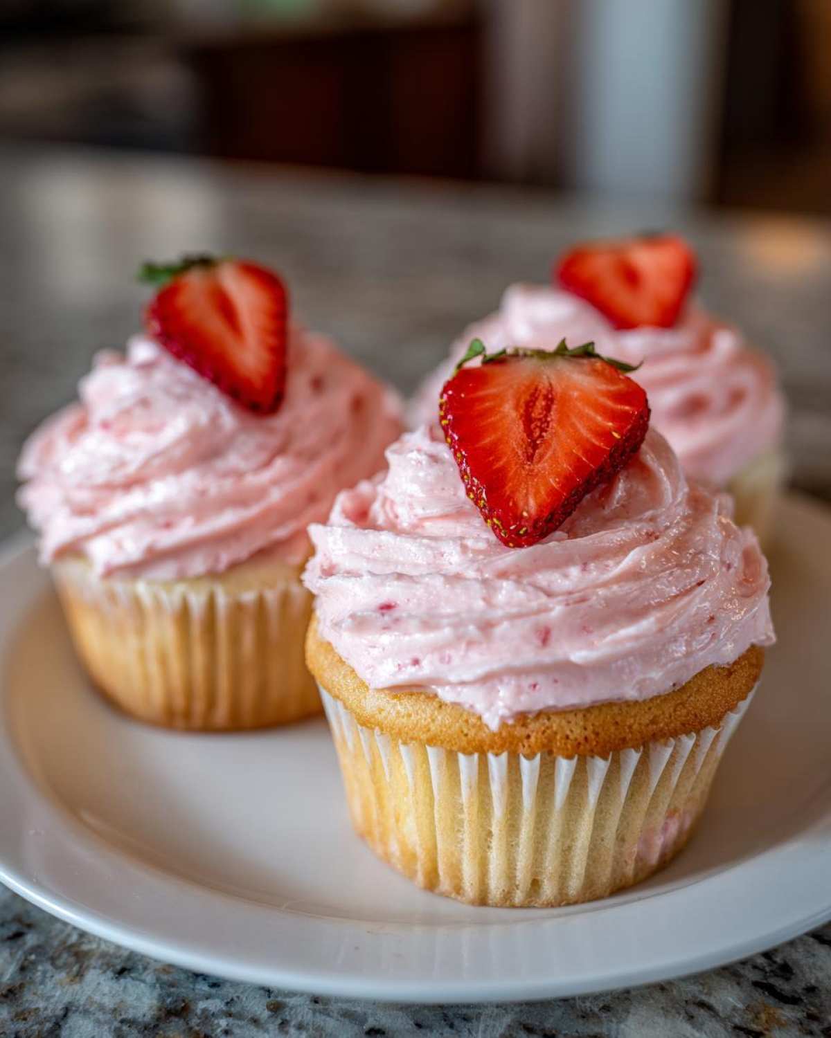 Three delicious strawberry cupcakes with pink frosting and fresh strawberry slices on top, ready to eat.