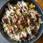 Close-up of a street corn chicken rice bowl featuring grilled chicken pieces, corn, rice, and a generous drizzle of white sauce.
