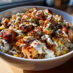 A close-up of a vibrant street corn chicken rice bowl topped with creamy sauce and paprika.