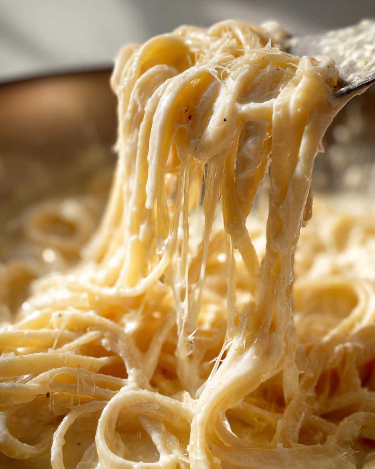 Close-up of fettuccine pasta being lifted, covered in thick, creamy homemade alfredo sauce with cheese pulls.