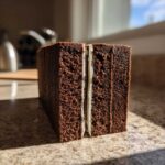 Close-up of thick, dark brown gingerbread house recipe dough layers separated by white icing.