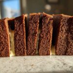 Close-up of thick, dark brown gingerbread house recipe slices layered with white icing.