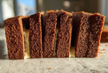 Close-up of thick, dark brown gingerbread house recipe slices layered with white icing.