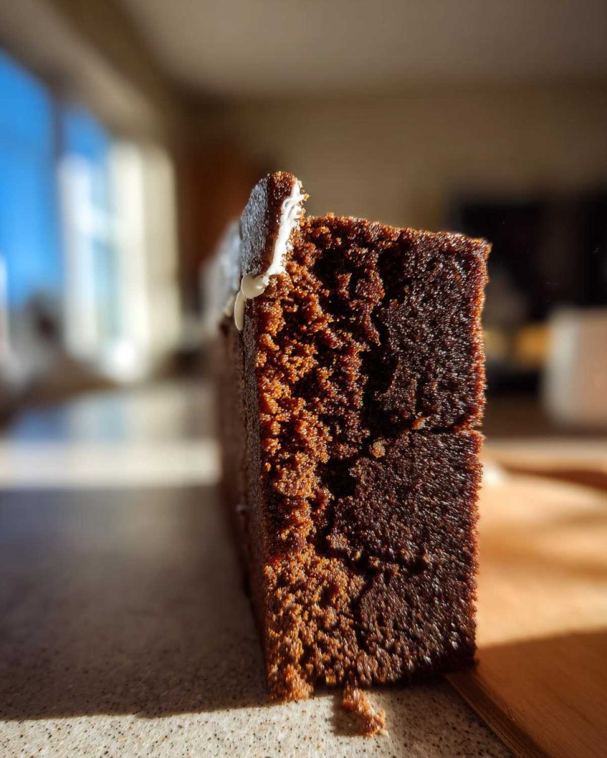 Close-up of a thick, dark brown piece of gingerbread house recipe dough or cake with a dab of white icing on top.