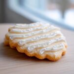 Close-up of a scalloped sugar cookie decorated with piped white lines from a sugar cookie icing recipe.