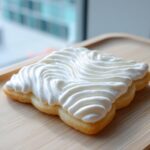 A close-up of a sugar cookie topped with thick, white piped icing using a star tip, showcasing the texture of the sugar cookie icing recipe.