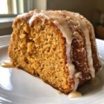 A close-up of a thick slice of sweet potato pound cake topped with a thick vanilla glaze dripping down the side.