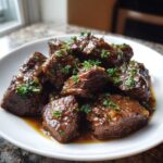 Close-up of tender, saucy crockpot steak cubes garnished with fresh chopped parsley on a white plate.